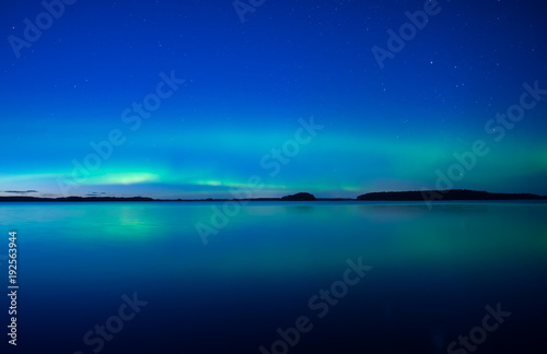 Northern lights dancing over calm lake. Farnebofjarden national park in Sweden