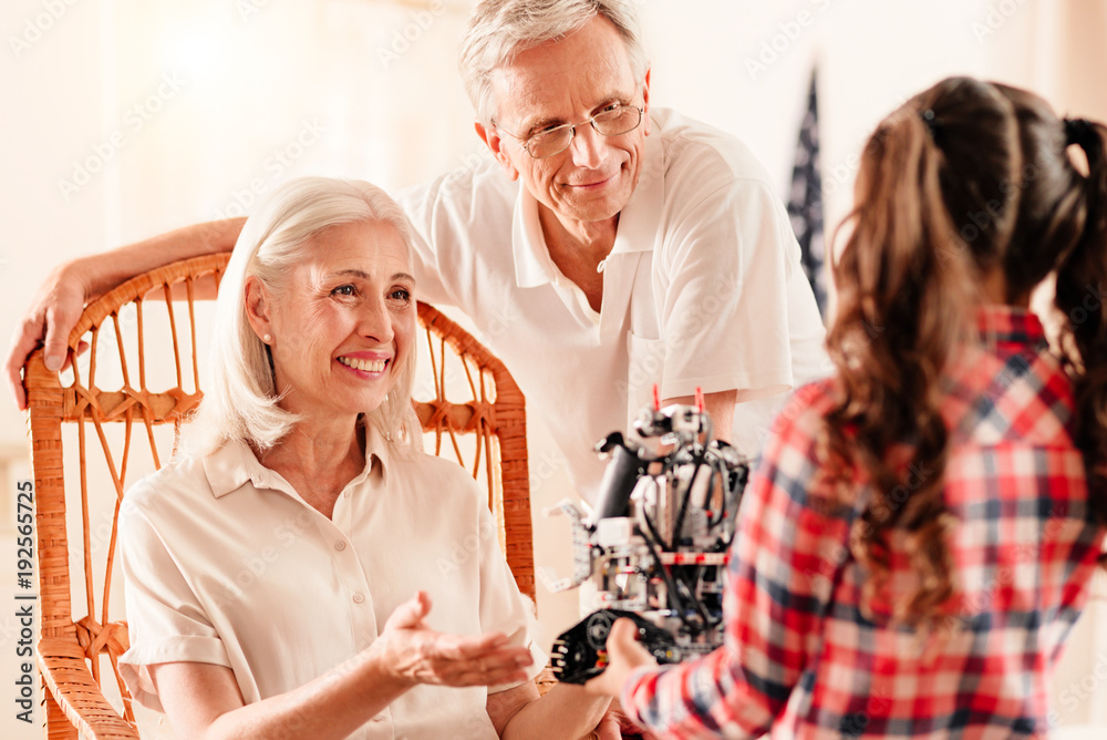 She is our everything. Selective focus on a happy retired couple grinning broadly while looking at their adorable granddaughter and listening to her story about robotic machines. She is our everything. Selective focus on a happy retired couple grinning broadly while looking at their adorable granddaughter and listening to her story about robotic machines.
