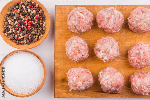 Raw meatballs on a wooden cutting board with ingredients - top view