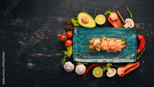 Tiger prawns on an avocado pillow and fresh vegetables. Top view. On a black wooden background. Copy space.