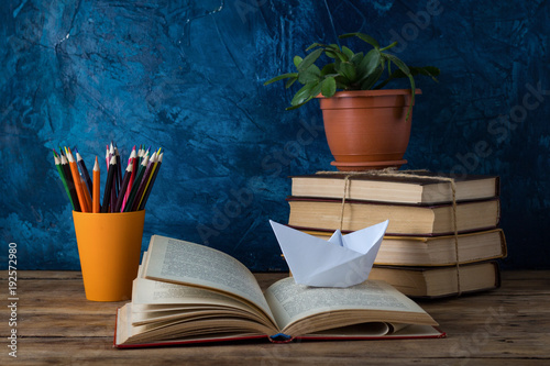 Open Book, A Pile of Books, A Paper Boat, Colored Pencils on a Darkly Blue Background