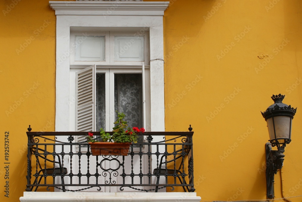 Beautiful white balcony with cast-iron balustrade and flower pot on yellow wall