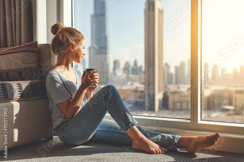happy young woman drinks coffee in morning at window photo