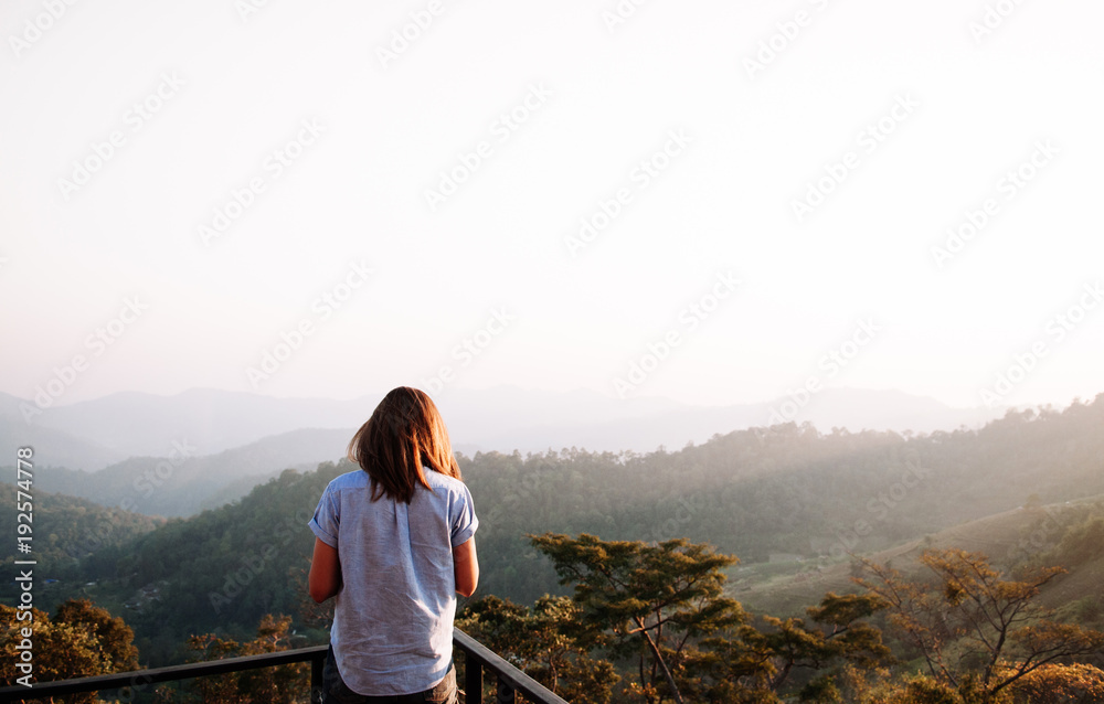 Naklejka premium Happy success woman at sunset or sunrise standing at mountain top looking to beautiful hills