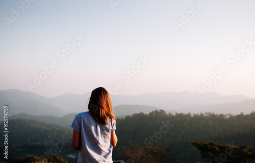 Happy success woman at sunset or sunrise standing at mountain top looking to beautiful hills