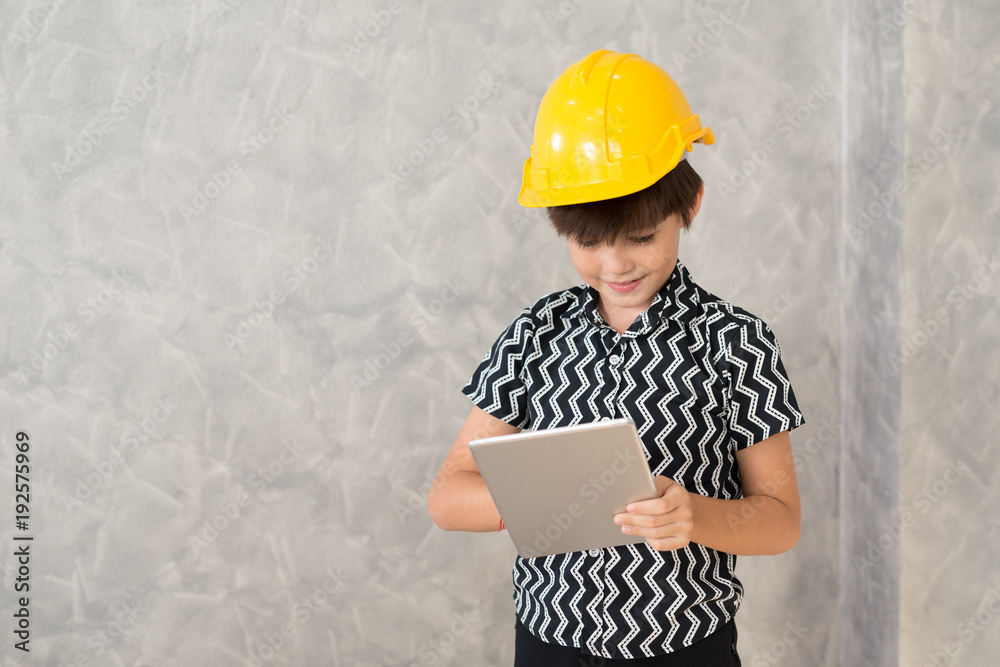 A boy wearing a yellow safety helmet are working with a digital tablet.. A boy wearing a yellow safety helmet are working with a digital tablet..