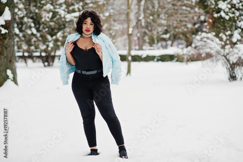 Stylish african american plus size model with mobile phone at hand at winter snowy day.