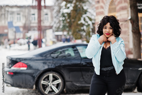 Stylish african american plus size model with mobile phone at hand  at winter snowy day against black car. © AS Photo Family