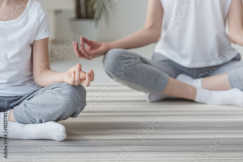 cropped shot of mother and daughter meditating in lotus pose together