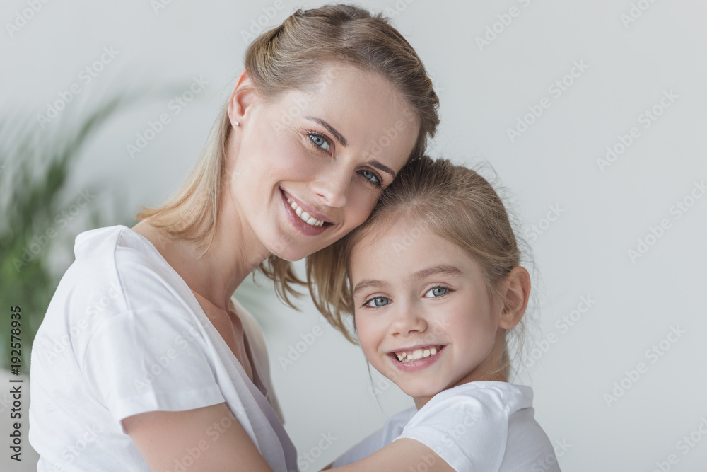 close-up portrait of mother and daughter embracing and looking at camera