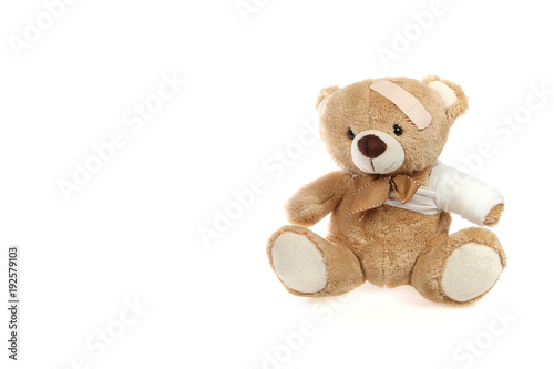 Teddybär mit Pfalster am Kopf und bandagiertem Arm vor weißem Hintergrund