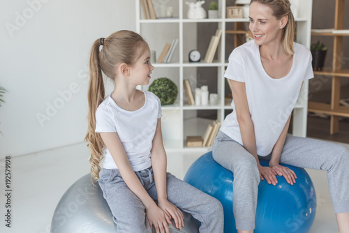 happy mother and daughter sitting on fit balls at home and looking at each other