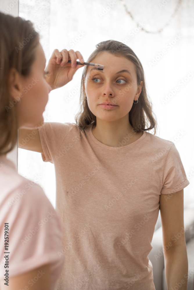 Portrait of attractive young woman putting on makeup at home. Eyebrow brush