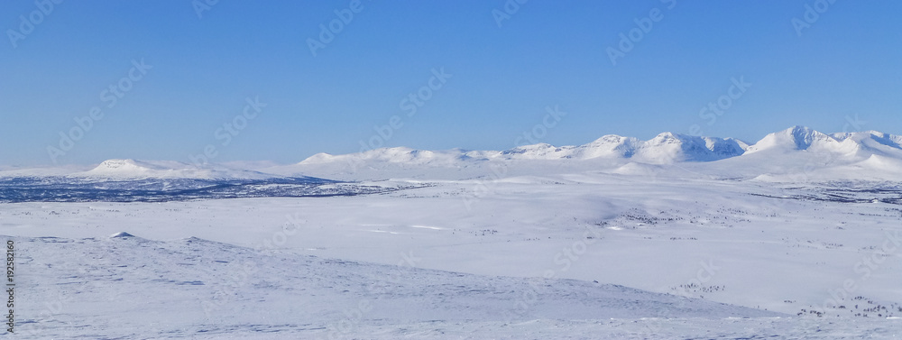 Large open field with snow and mountains on the horizon in northern Sweden near the polar circle.