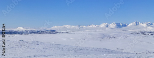 Fotografi Large open field with snow and mountains on the horizon in northern Sweden near the polar circle
