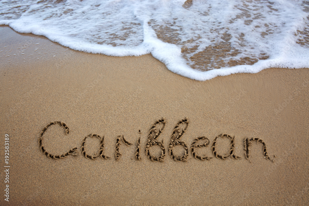 Fototapeta premium Word Caribbean written on the sand near the sea.