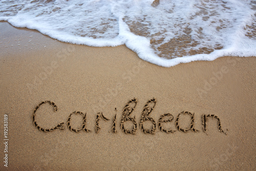 Word Caribbean written on the sand near the sea.