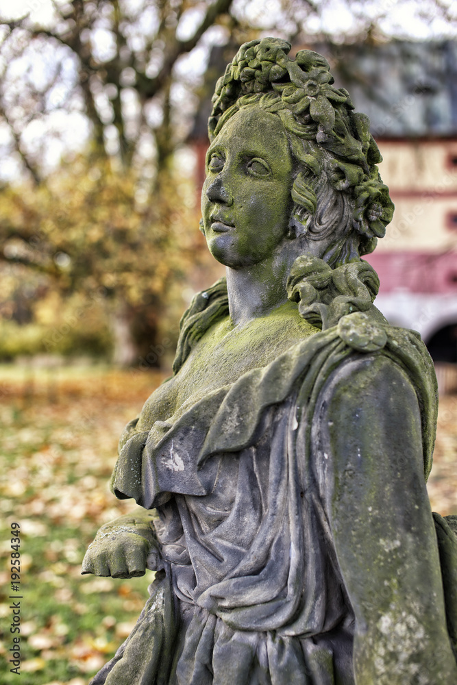 Side detail of old  green moss covered statue of the girl with flowers in her hair