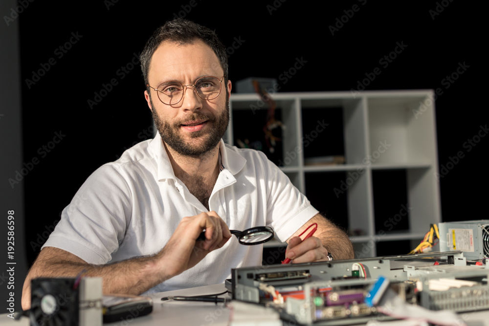 man in glasses looking at camera while he fixing pc