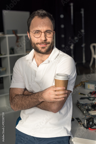man with coffee in hand looking at camera while leaning on table