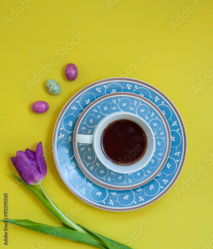 A floral blue tea set on yellow background with chocolate ehhs and a tulip flower. Flat-lay. Negative space. photo