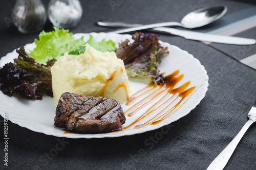 On a white plate, on a beautiful fabric and dark background mashed potatoes with beef meat beautifully polished balsamic sauce