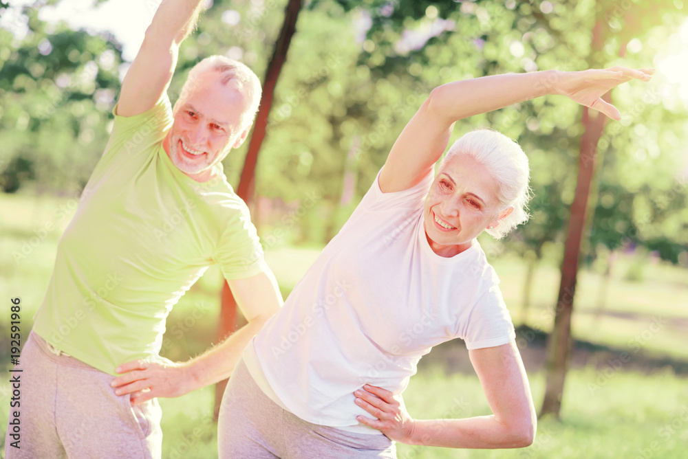 Older and healthier. Waist up of positive friends looking away while doing useful exercises outdoors and having fun