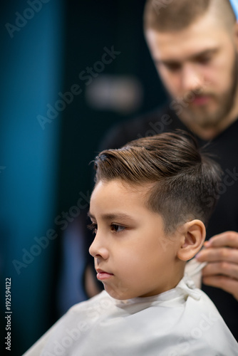 The  young man the hairdresser does a hair to the schoolboy
 in hairdressing salon. The hairstyle is ready. photo