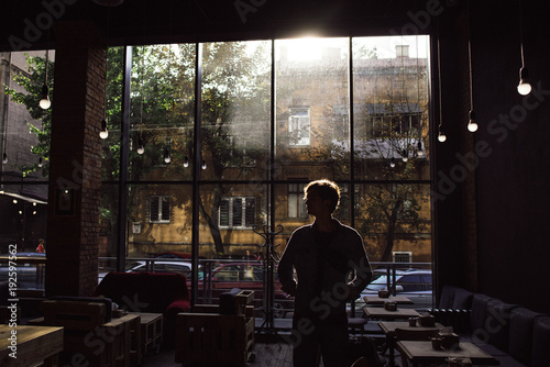 Man standing on empty cozy cafe with sunlight back view