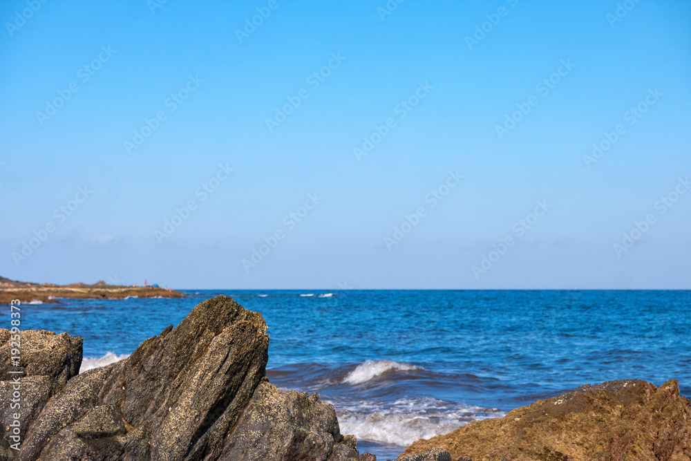 Closeup of rocks with azure ocean and clear blue sky in the background