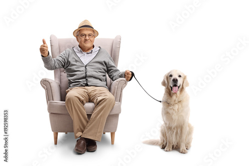 Mature man with a labrador retriever dog sitting in an armchair and making a thumb up sign