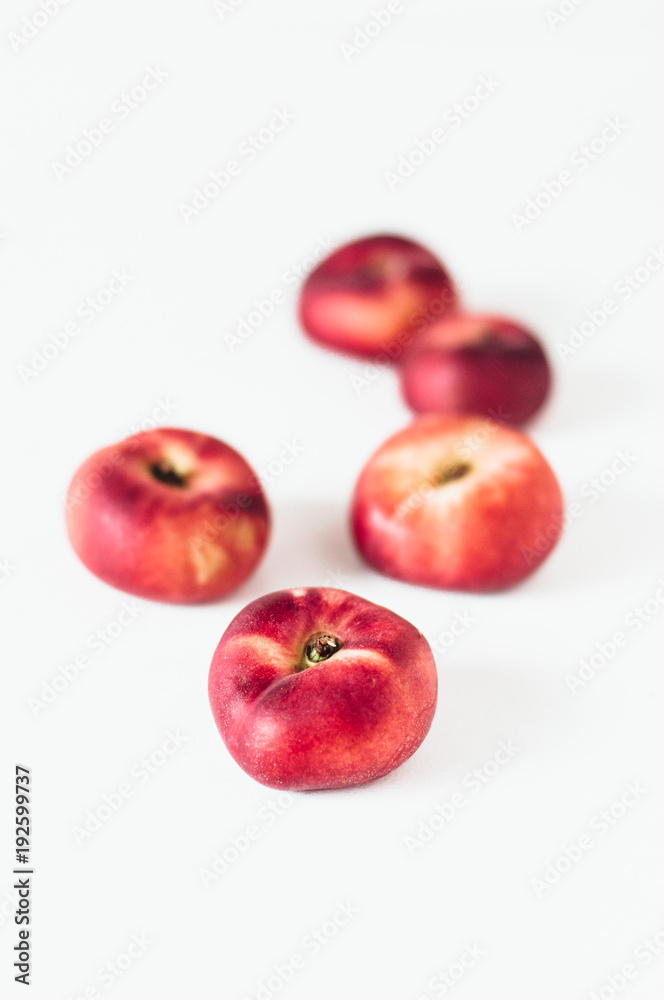 Selective focus composition of several fresh flat donut nectarines, red saturn nectarines or ripe fuzzless vineyard peaches on white background Selective focus composition of several fresh flat donut nectarines, red saturn nectarines or ripe fuzzless vineyard peaches on white background