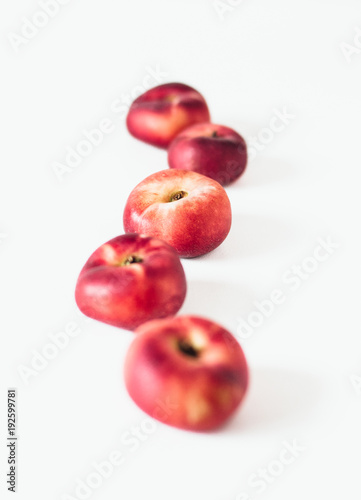 Selective focus composition of several fresh flat donut nectarines, red saturn nectarines or ripe fuzzless vineyard peaches on white background