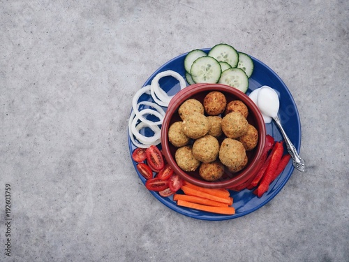 Tasty homemade falafel balls with assorted vegetables and low fat vegan yogurt on a colorful plate and concrete stone background. Halal food, vegetarian meal. Middle eastern snack. Space for text.