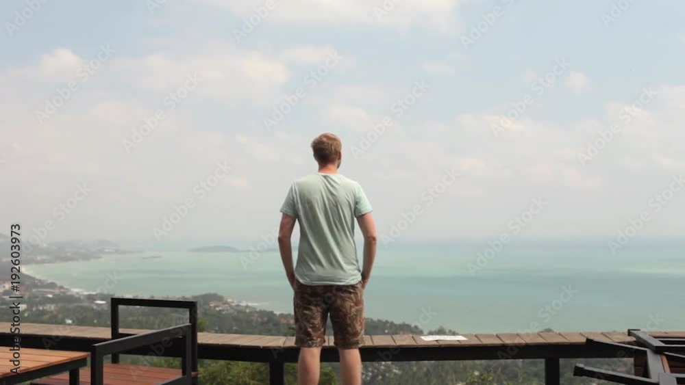 man is standing on a cliff overlooking a tropical island man is standing on a cliff overlooking a tropical island