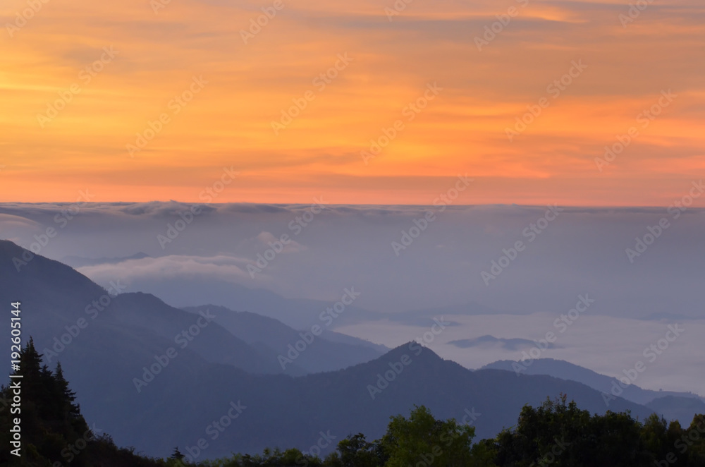 orange sky in the morning over a cloud layer and mountain with a fog cover on a basin in a valley