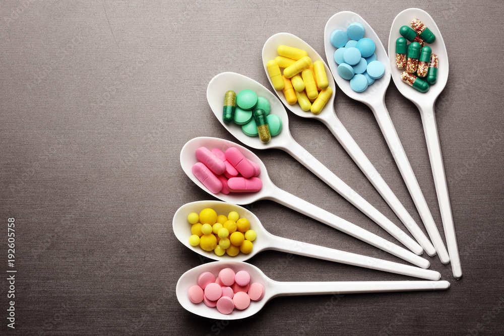 Colorful pills in plastic spoons on a grey background Colorful pills in plastic spoons on a grey background