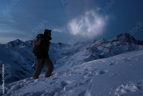 Extreme tourism. Brave expeditor lights the way with a headlamp at night winter mountains. Man with backpack commit climb on snowy slope in high ridge. Ski tour