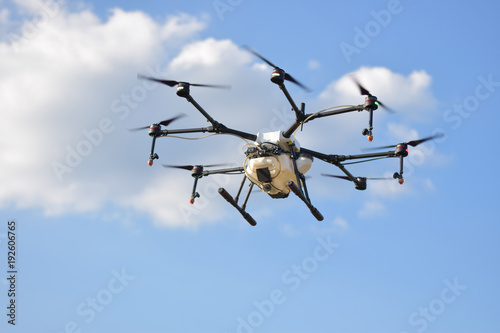 Flying agriculture drone, photo image of agriculture drone carry a tank of liquid fertilizer flying in the blue sky prepare to spray it in farming area, agriculture technology, drone technology