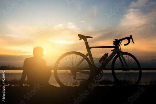 A man sitting beside a bicycle in the morning.
