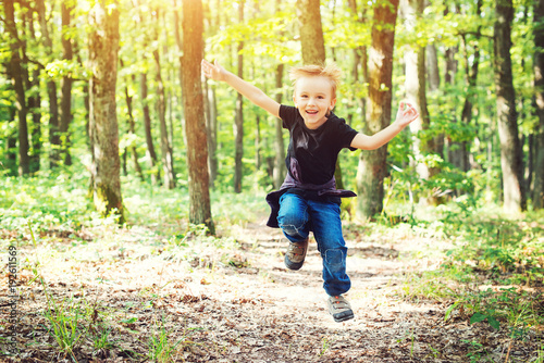 Happy blond boy jumping in sunny day on nature.