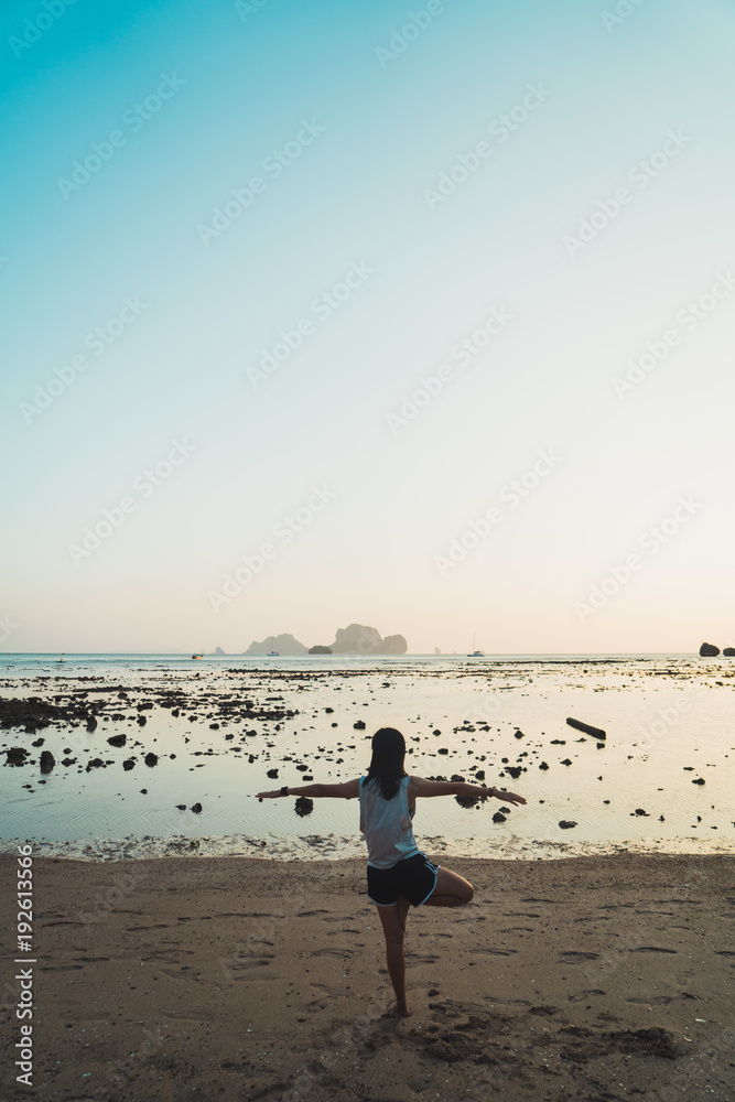 Sportive woman balancing on beach practicing yoga