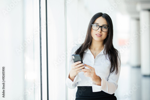 Portrait of a young business woman in glasses typing text phone against panoramic windows. Business concept © F8  \ Suport Ukraine