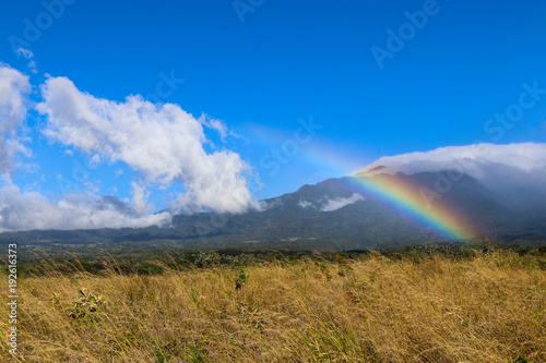 Rainbow over grassy field with mountain and clouds in background