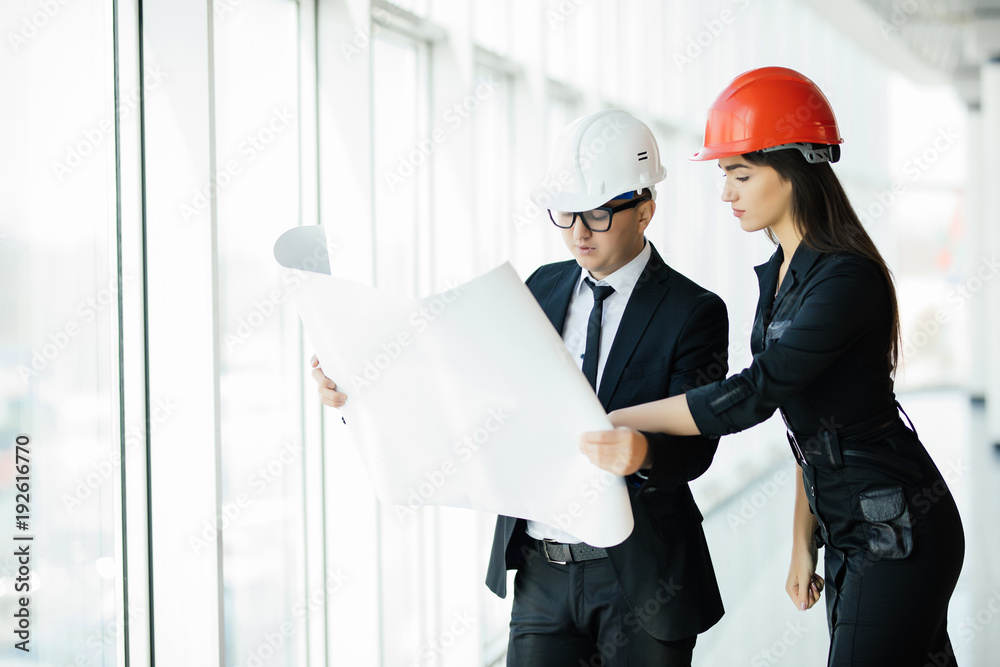 The man and woman in a helmets hold the project plan in the building. Construction business. The man and woman in a helmets hold the project plan in the building. Construction business.