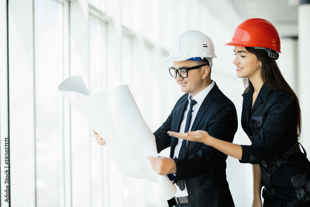 Businessman architects look at paper plan business woman architect in office to discuss business projects near panoramic window. Businessman architects look at paper plan business woman architect in office to discuss business projects near panoramic window.