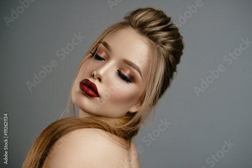 Beautiful blonde girl with professional make-up and hairdo in studio on gray background