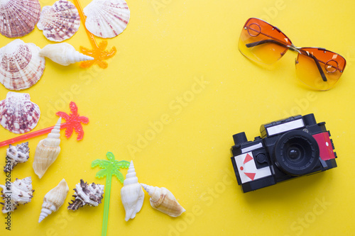 Bright yellow one-color background with old vintage camera, sea shells, sunglasses, top view. Travel or tourism concept. Space for a text or product display.