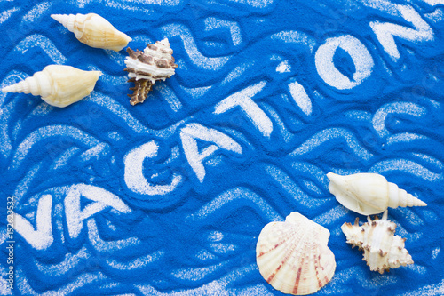 Vacation inscription on a blue colored sand with waves, sea shells, top view, flat lay photo