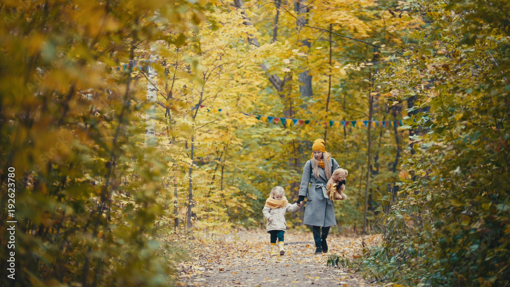Fototapeta premium Pretty blonde little daughter with her mommy walks in autumn park - have funny and collect leaves